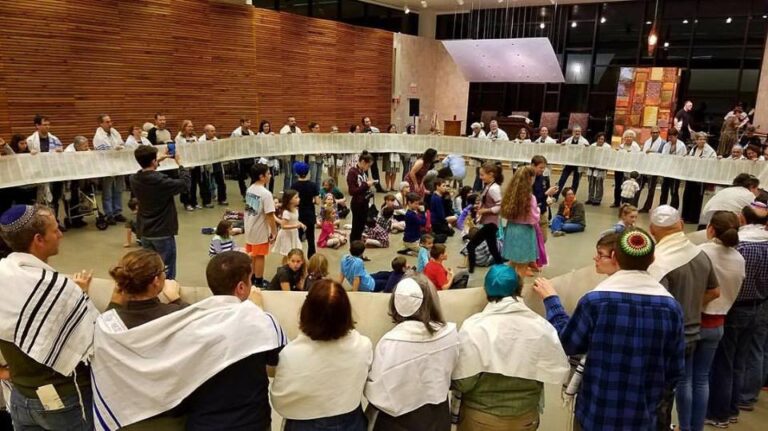 adults in tallitot and kipot holding unrolled Torah scroll around children