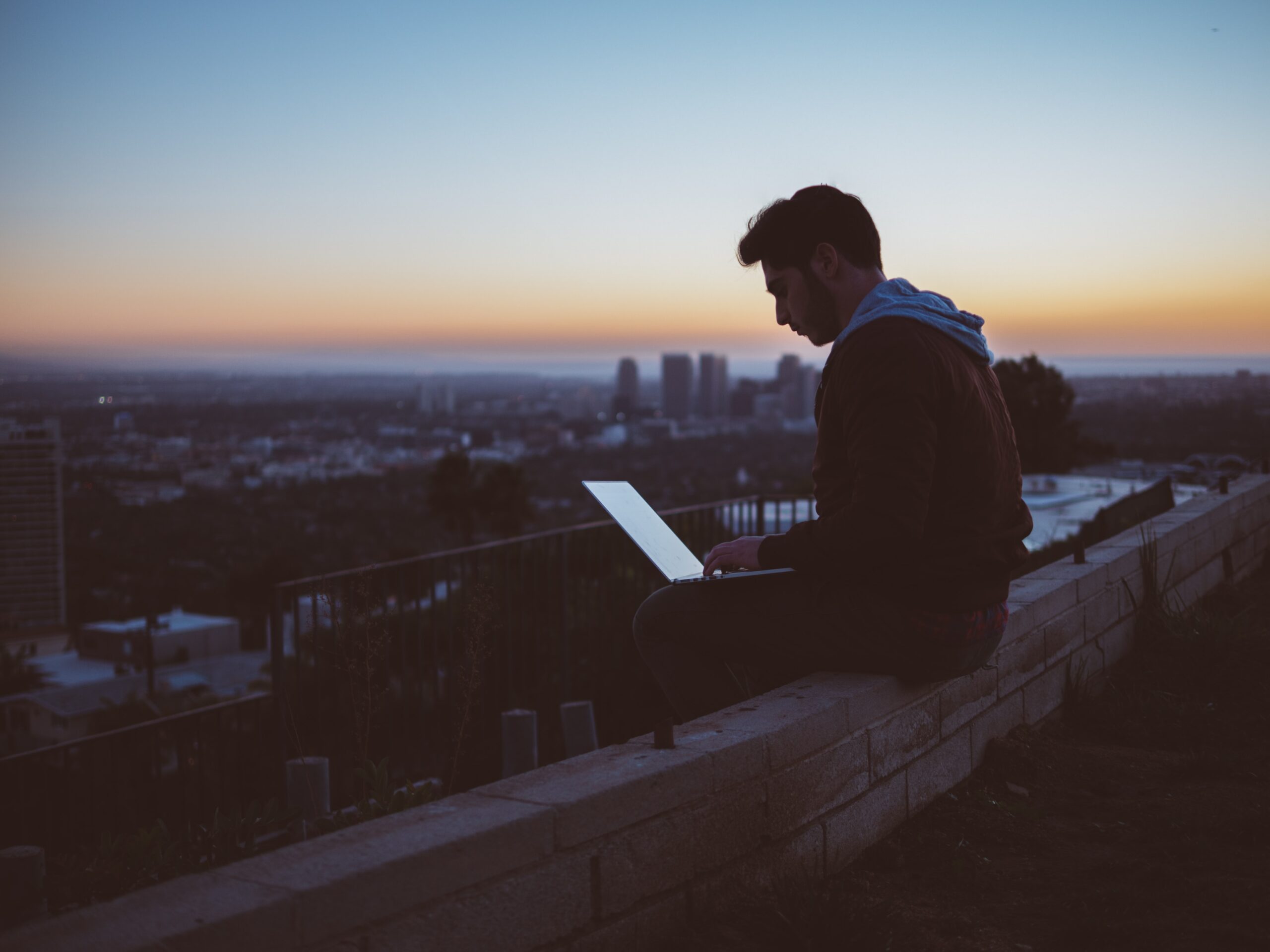 person sitting on balcony above city, working on laptop