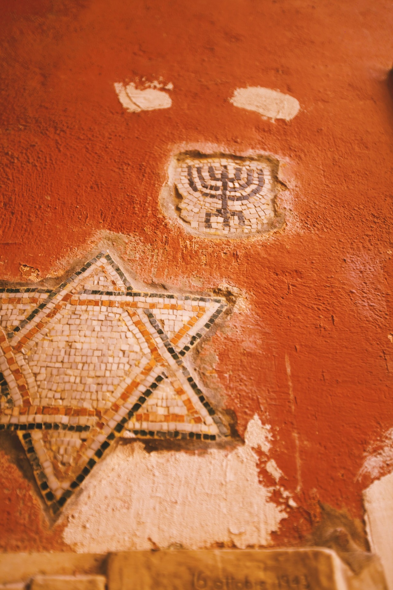 Mosaic Star of David and menorah on a textured, faded red wall.