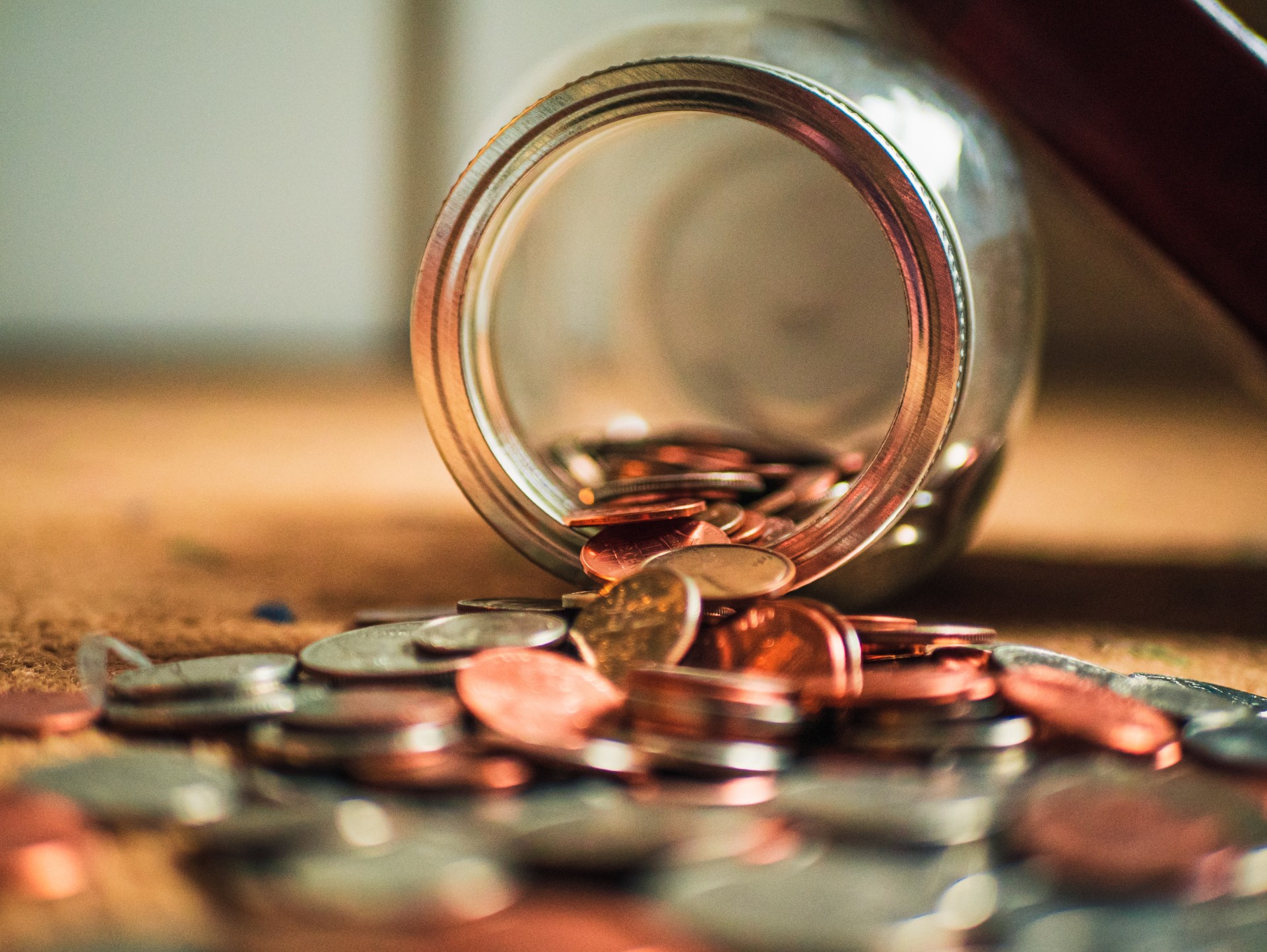 Coins spilling from a glass jar onto a table.