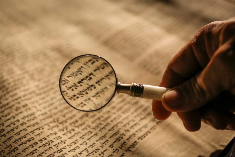 hand holding magnifying glass to Hebrew text