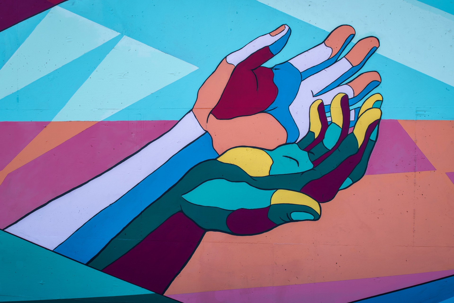 Colorful mural of two outstretched hands against a background of geometric shapes in shades of blue, orange, and pink.