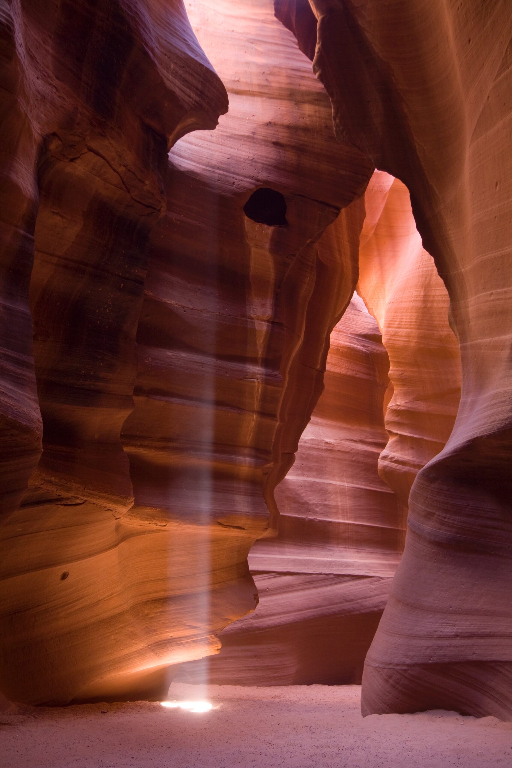 Sunlight beams through narrow, wavy rock formations in a sandstone slot canyon.
