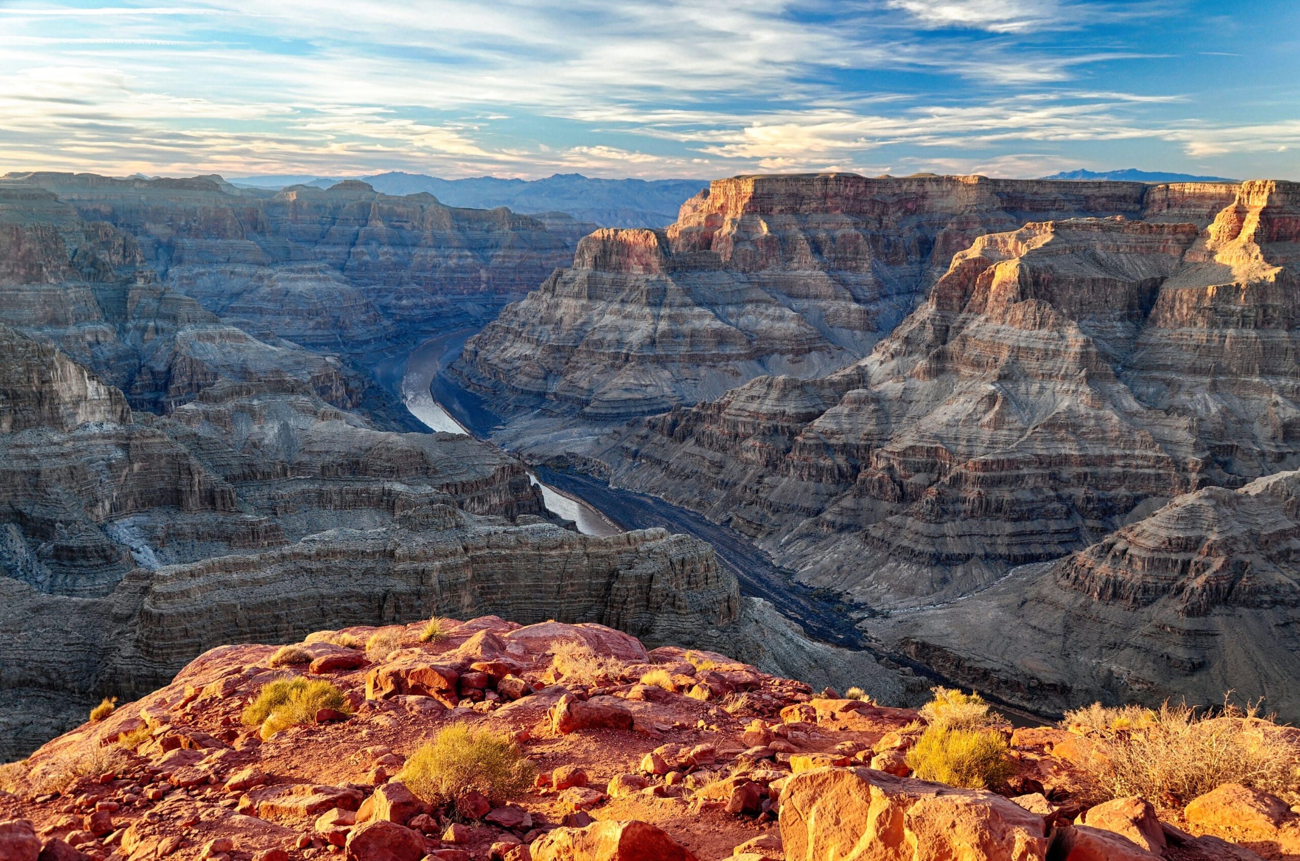 Vista of the Grand Canyons layered rock formations and winding river under a partly cloudy sky.