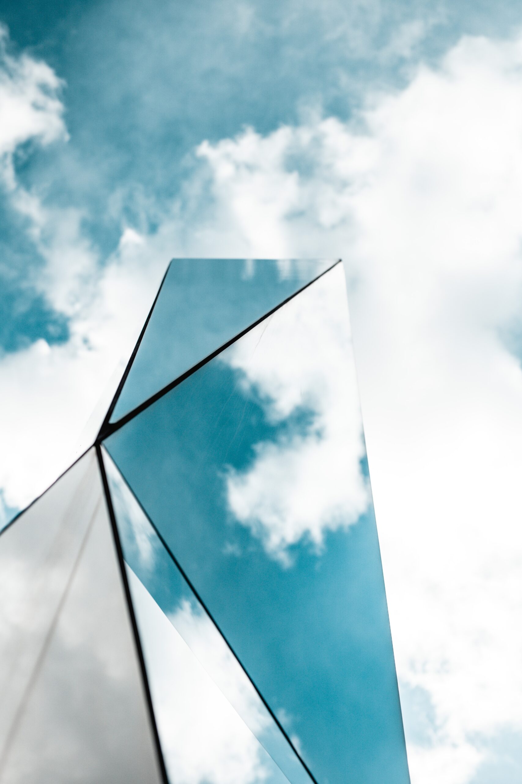 Tall reflective glass structure against a blue sky with scattered clouds.