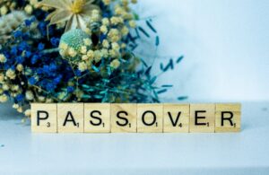 Scrabble tiles spelling Passover with a floral arrangement in the background.