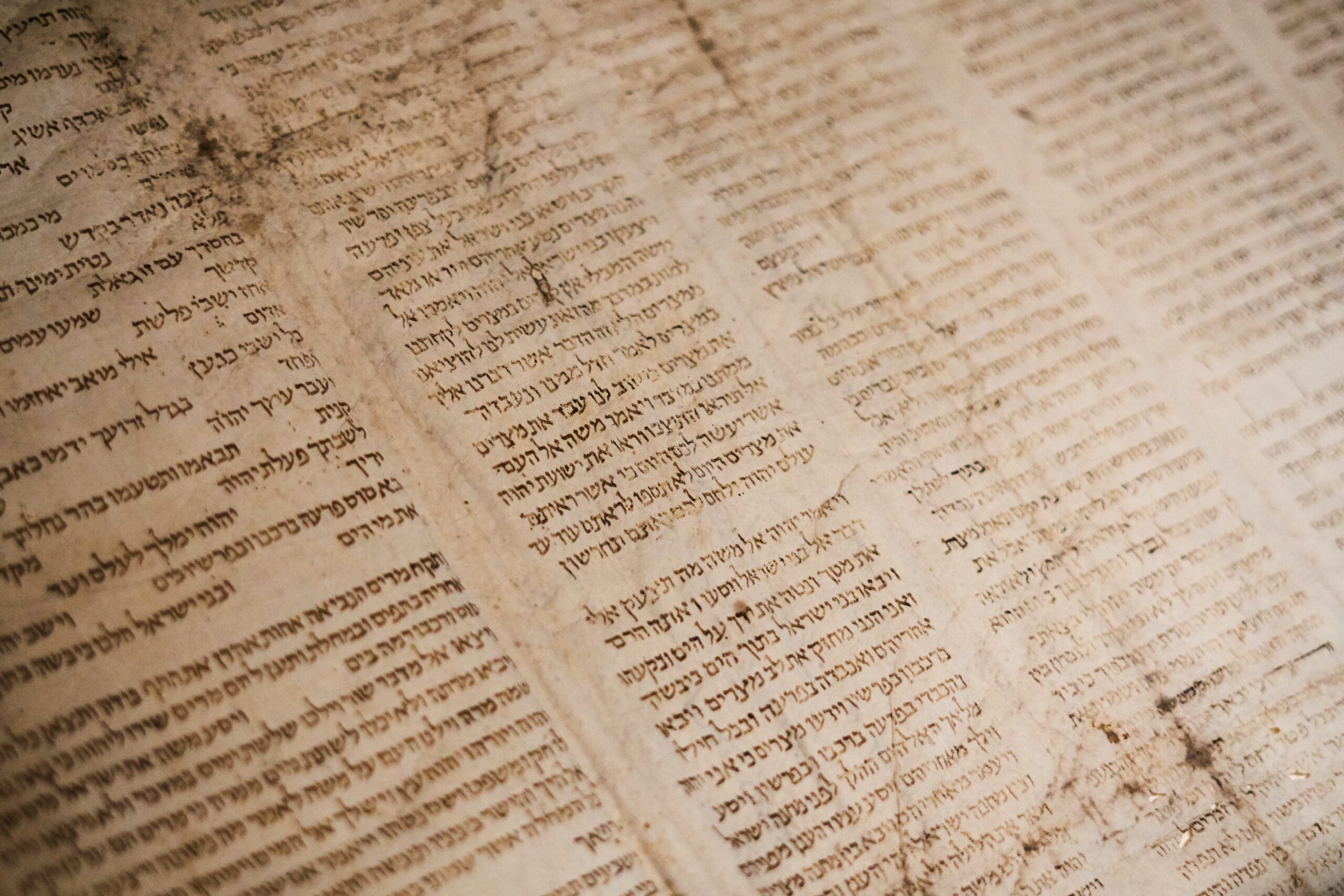 Close-up of an ancient, weathered manuscript with Hebrew text arranged in vertical columns.