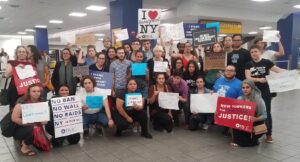 A group of diverse people holding signs supporting immigrant rights in a public indoor space.