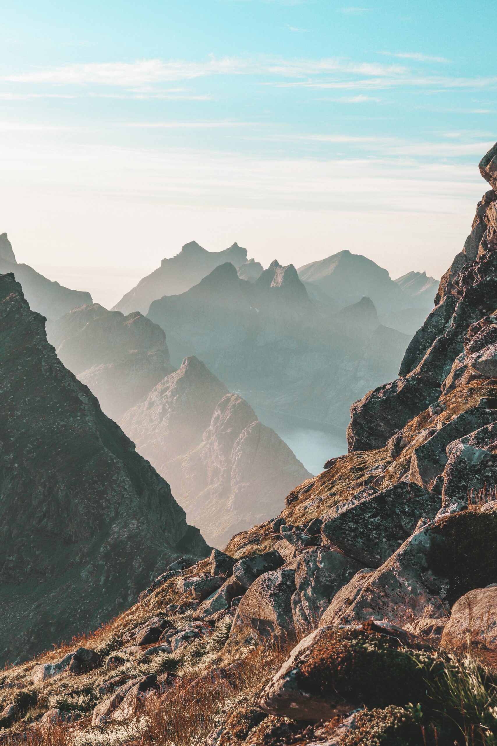 Mountain peaks with mist and rugged rocky terrain under a blue sky.