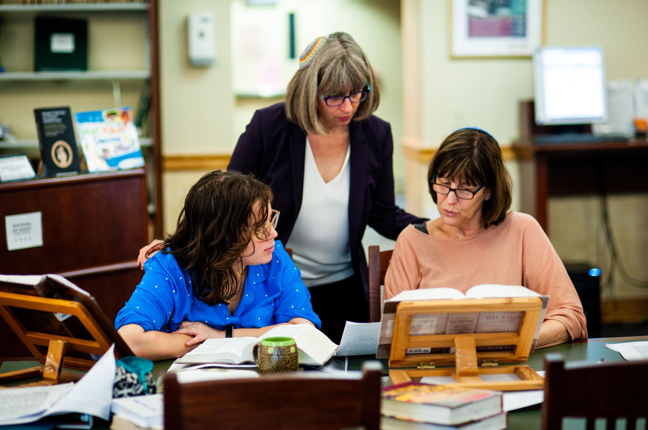 Three women sitting at a table in a library, reading books and discussing.