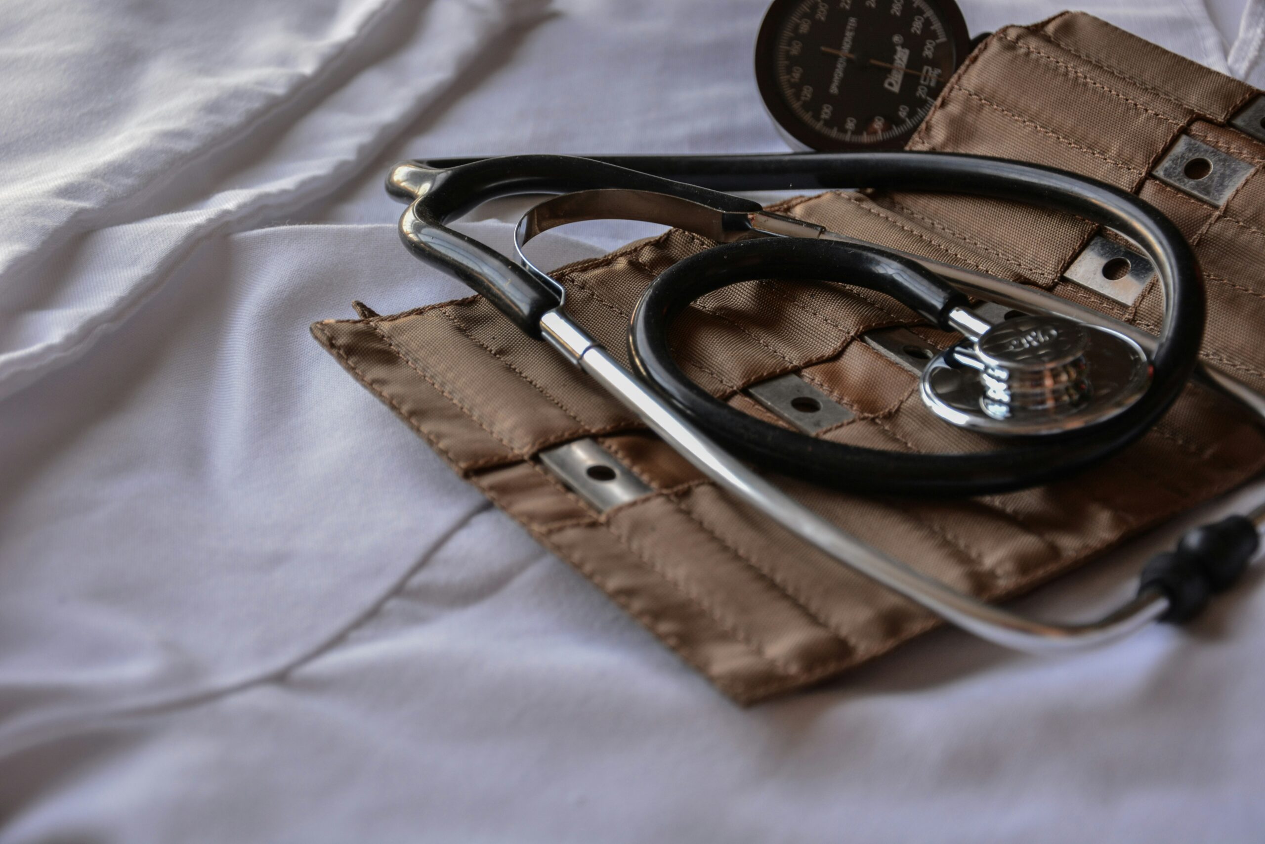 A stethoscope and a blood pressure cuff on a white surface, partially in a brown case.