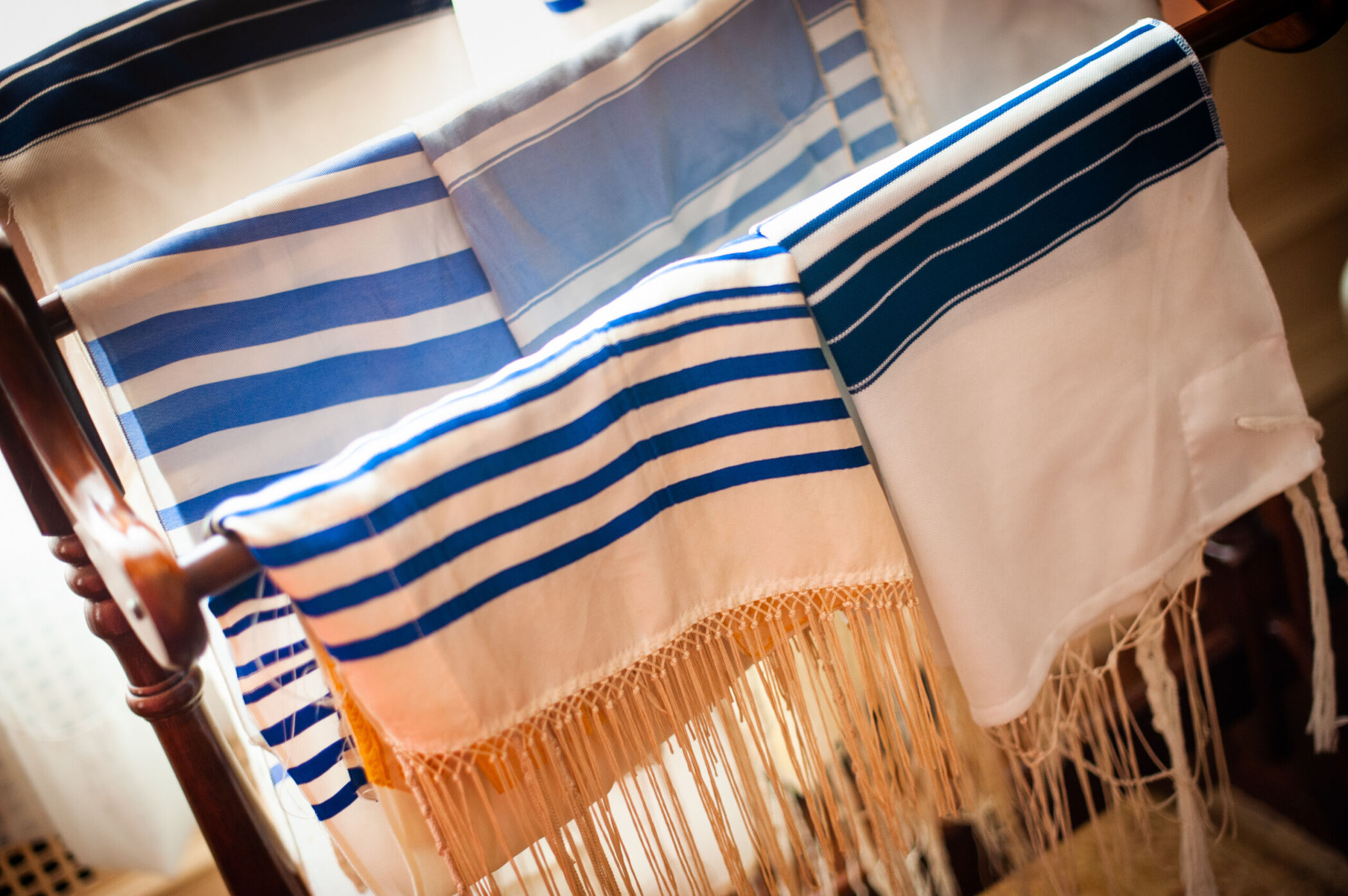 Colorful prayer shawls with blue stripes are draped over a wooden rack.