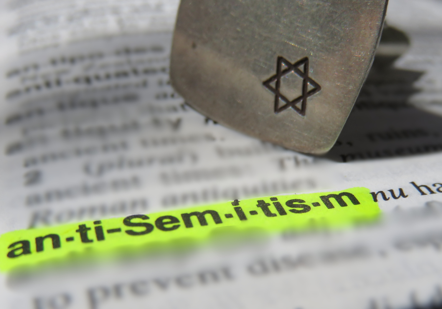 The word antisemitism is highlighted in a dictionary, next to a Star of David stamp.
