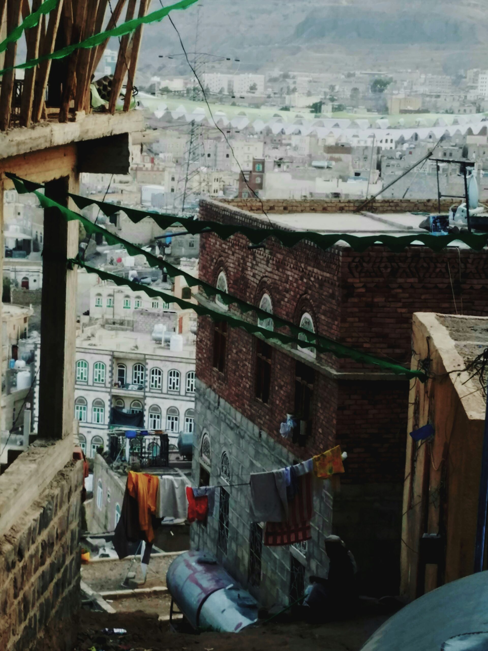 Narrow alleyway with colorful clothes hanging, brick buildings, and a hilly cityscape in the background.