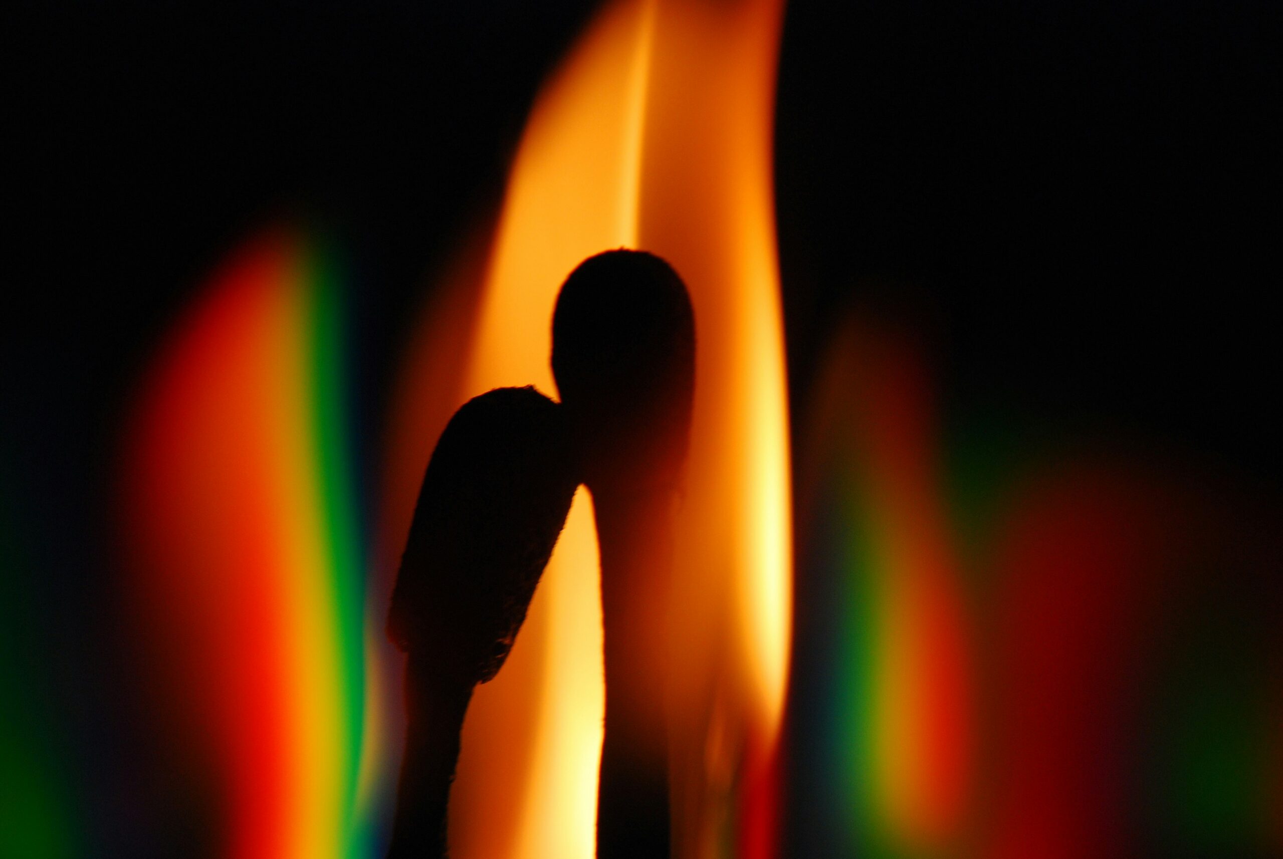 Silhouettes of two matchsticks with a colorful, blurred flame background.