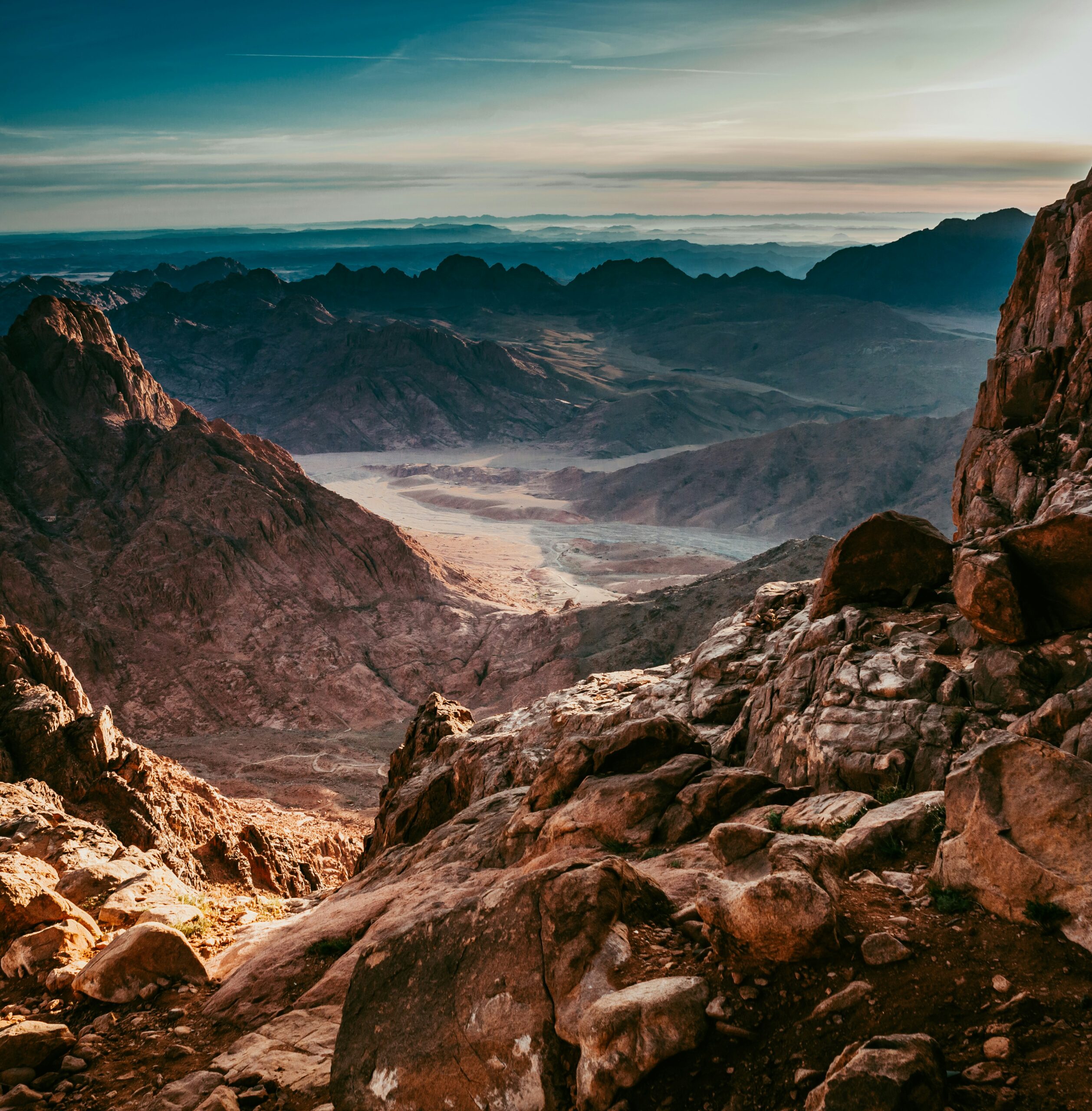 Rocky mountain landscape with a valley below under a dramatic sky at sunrise or sunset.