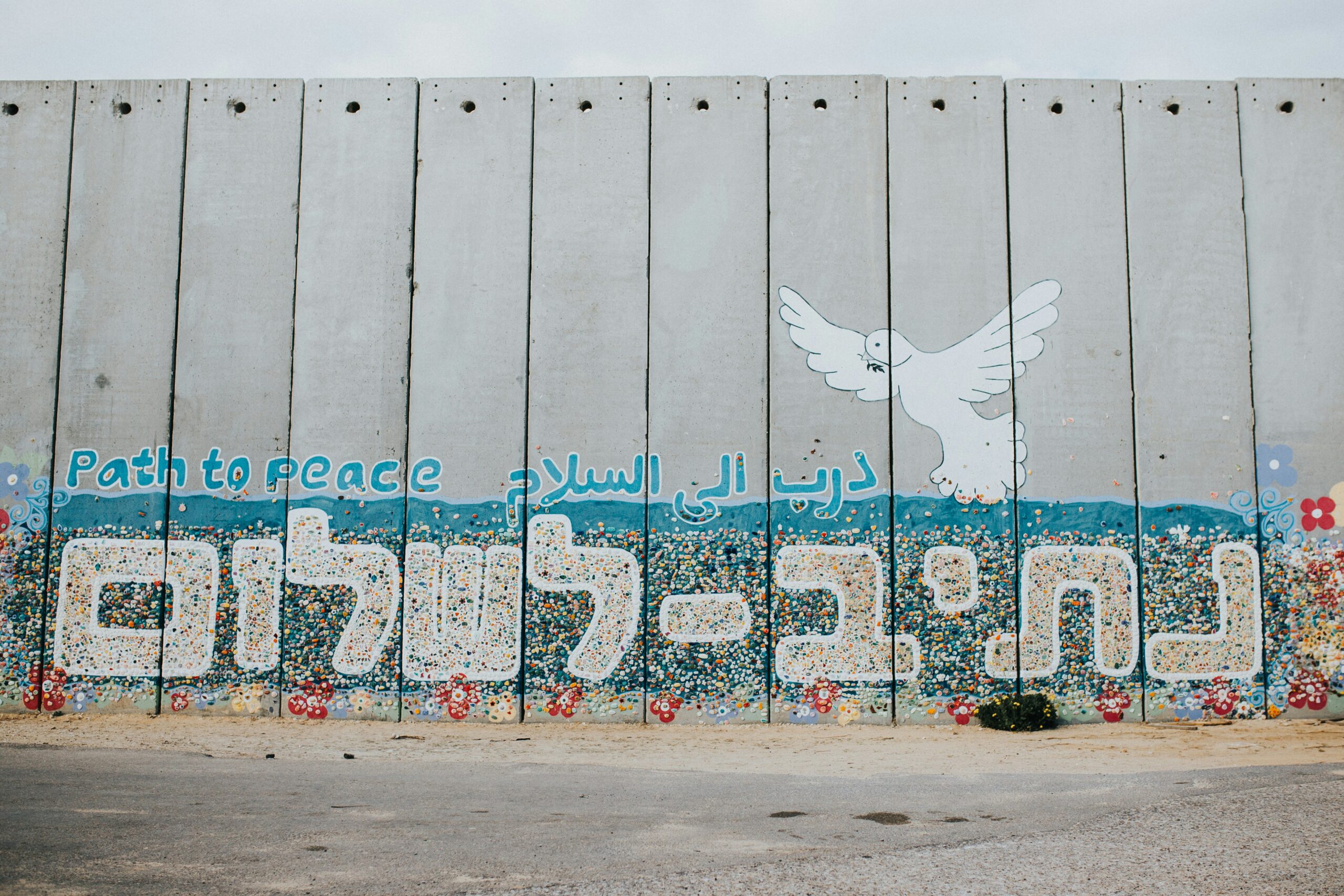Graffiti on a wall with a white dove and the phrase Path to Peace in multiple languages.