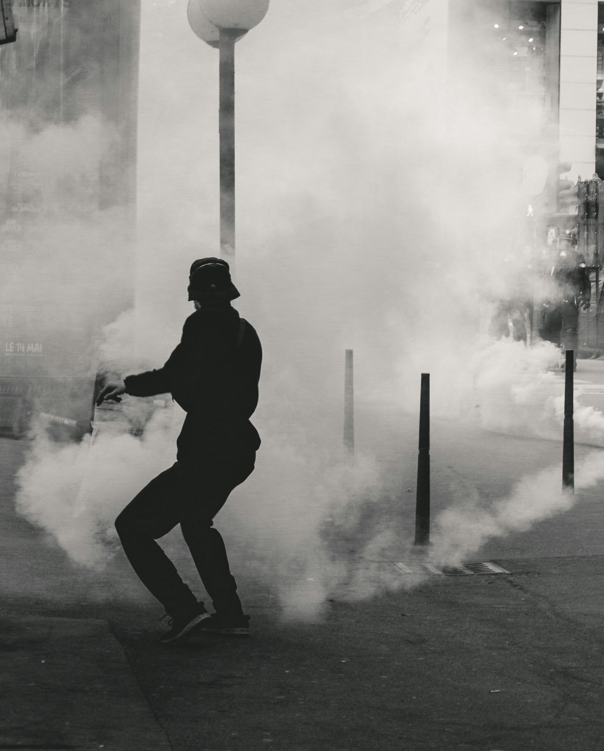 Person in hat and jacket runs through thick smoke on a city street.