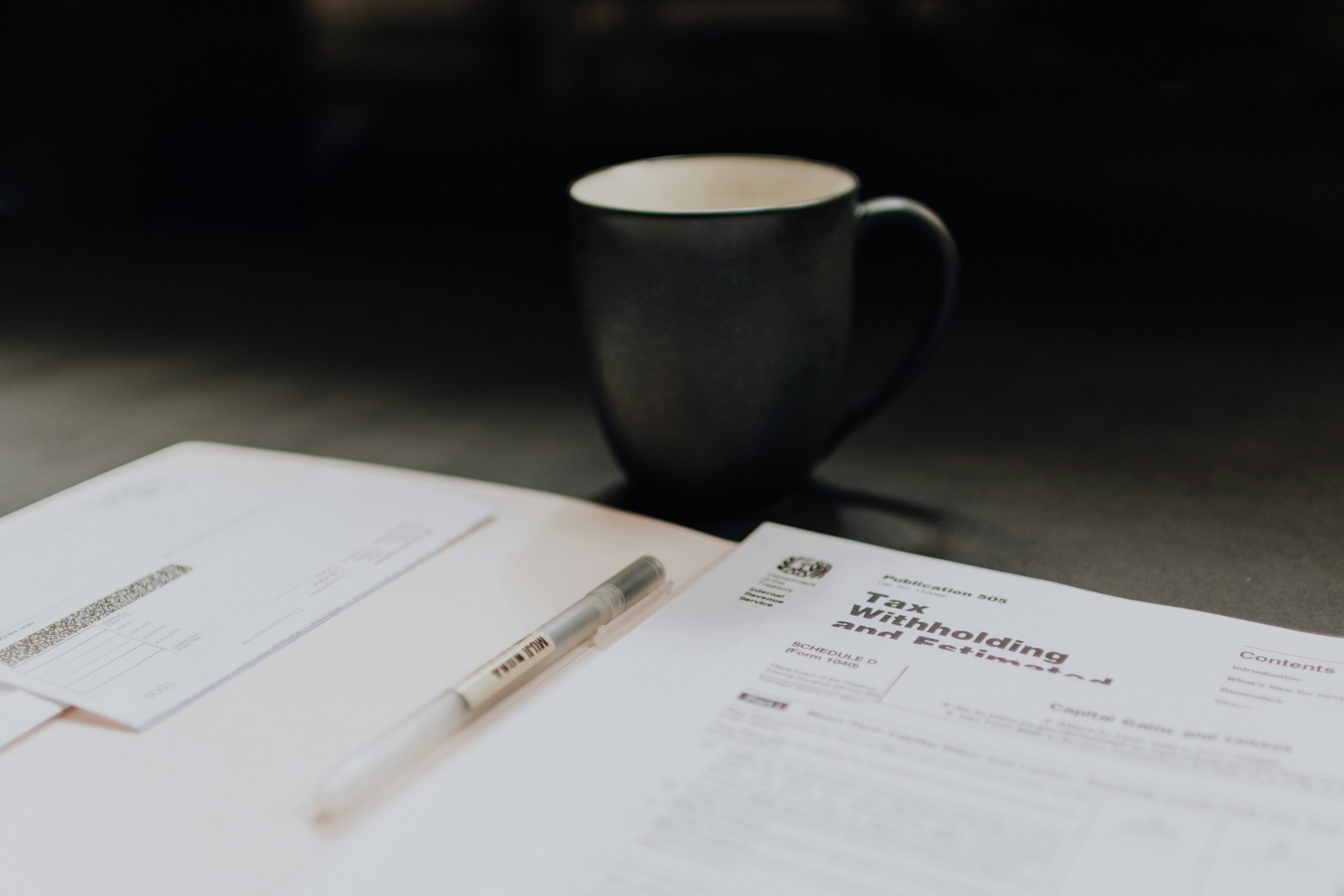 A coffee cup next to tax withholding forms and a pen on a table.