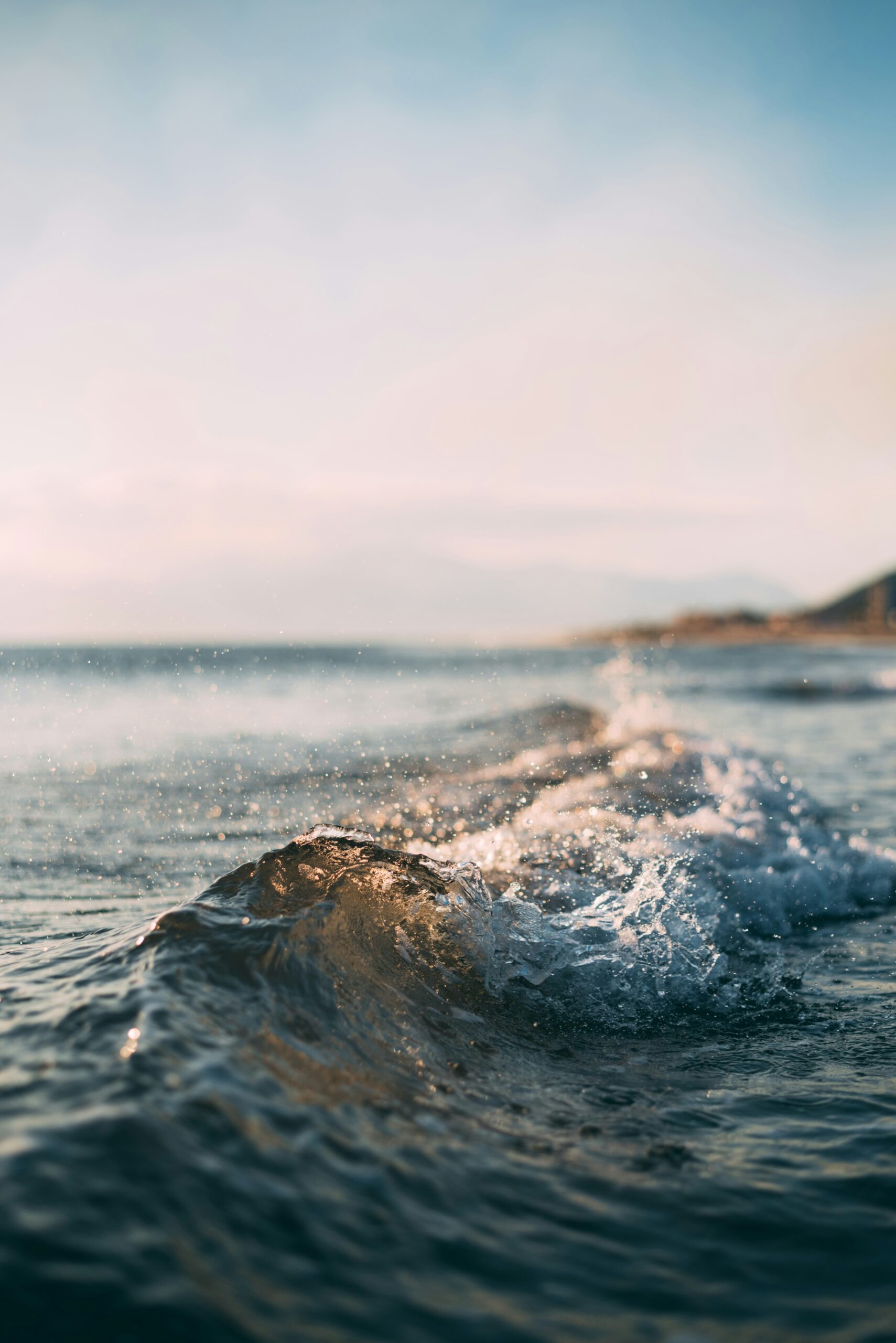 Gentle waves crashing on the shore under a clear sky, with distant mountains in the background.