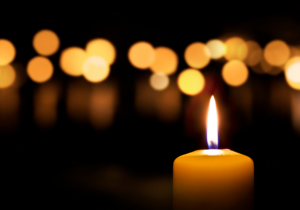 A single lit candle with a bokeh background of soft, out-of-focus, warm lights in the dark.