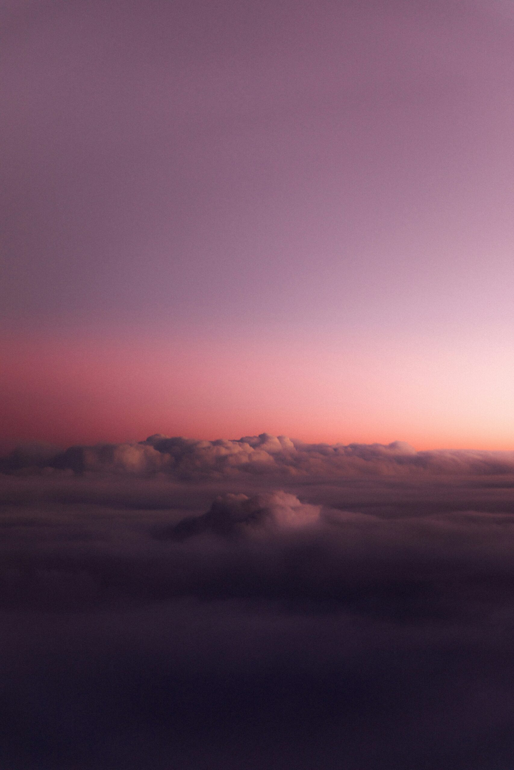 A serene view of a mountain peak emerging through soft clouds at sunset, with a purple and orange sky.
