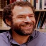 Smiling man with a beard in front of bookshelves.