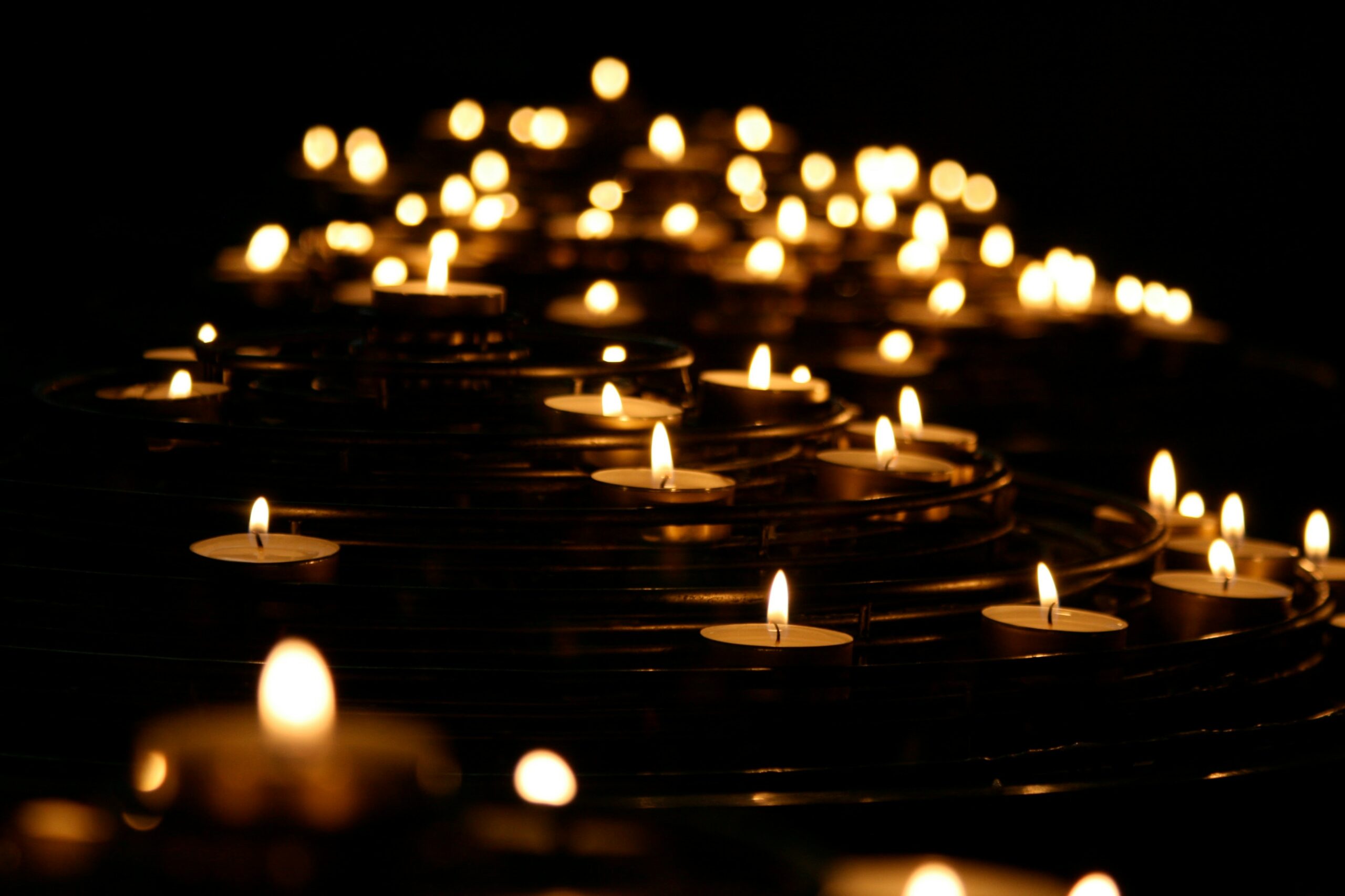 Numerous candles glow softly in a dark setting, creating a warm and serene atmosphere.