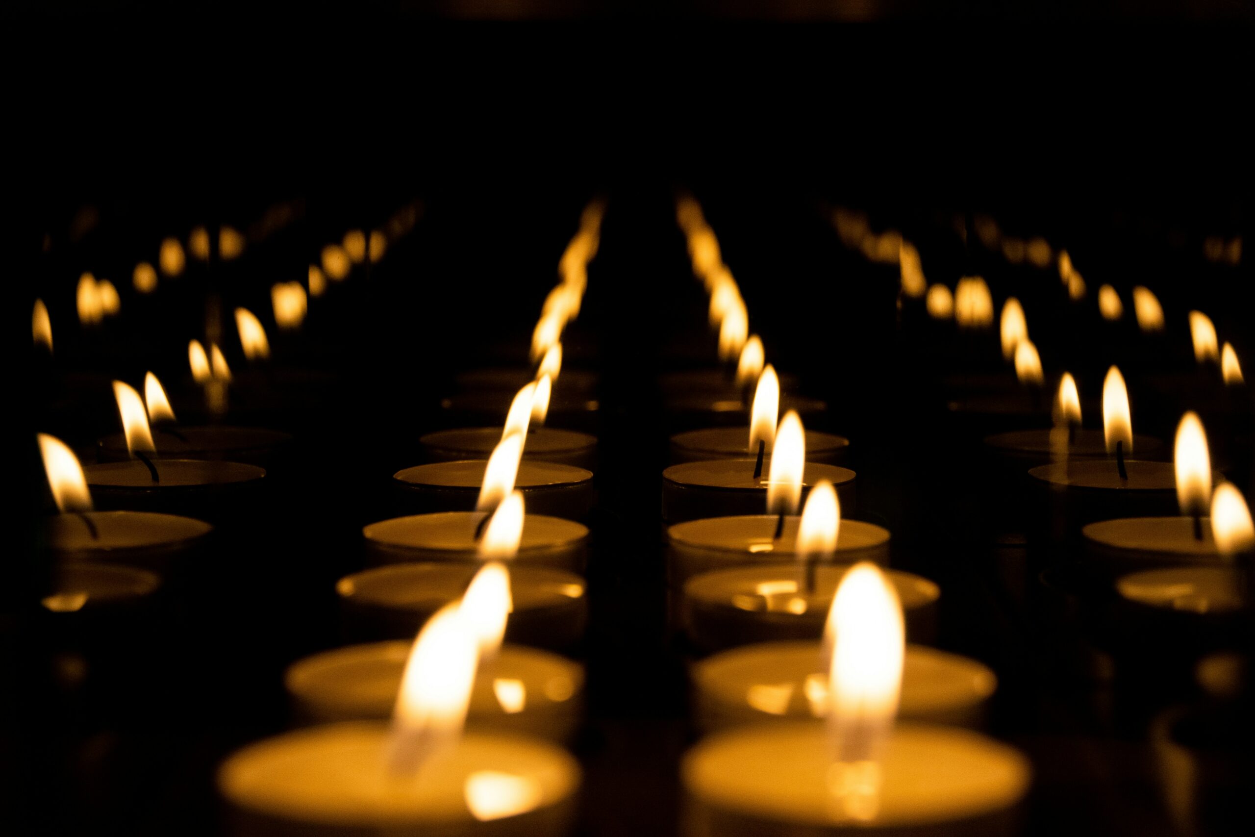 Rows of lit candles creating a warm, glowing ambiance in a dark setting.