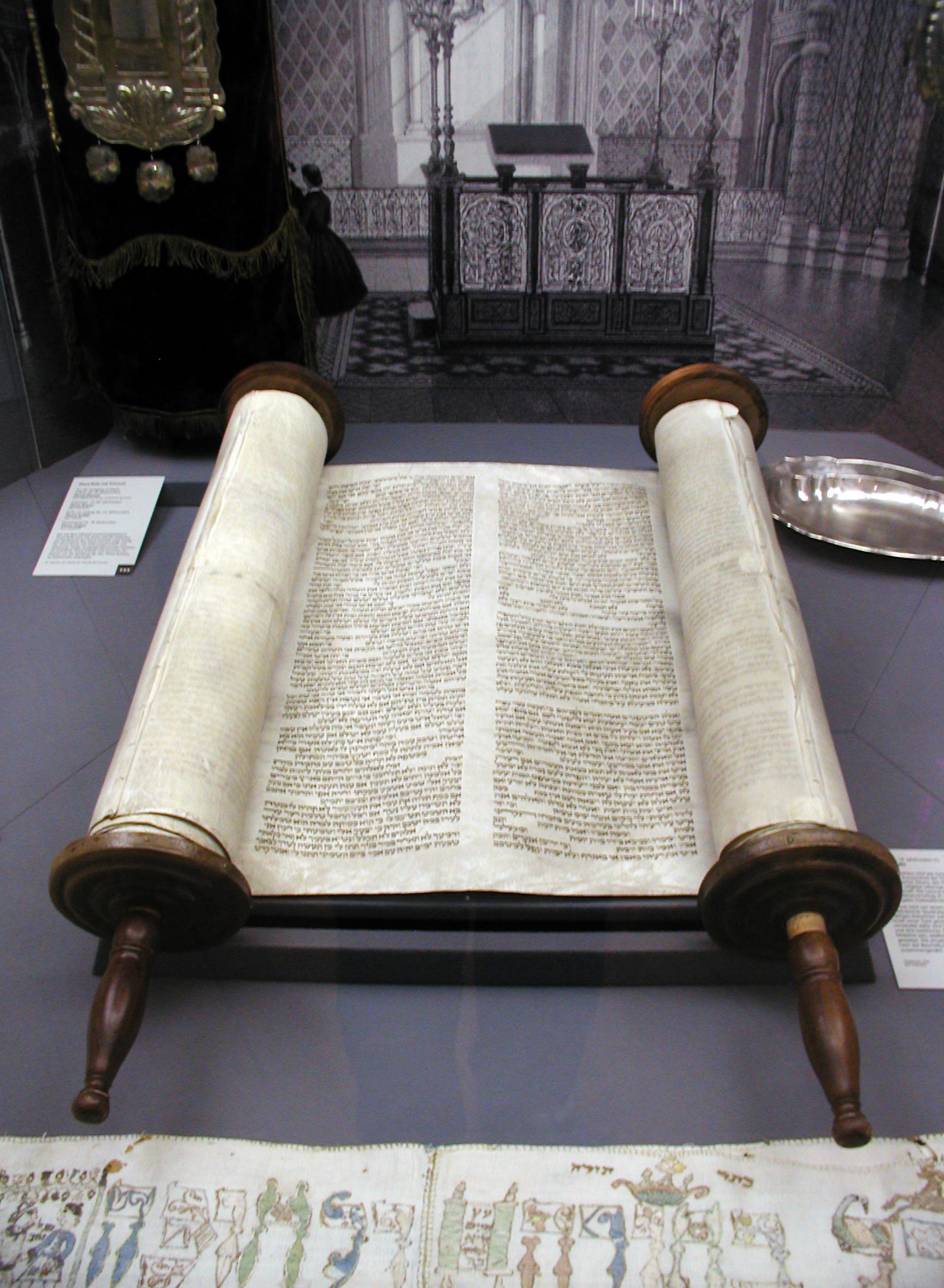 An open Torah scroll displayed on a stand with a decorative backdrop.