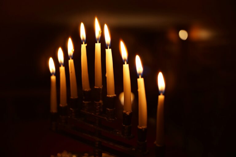 Nine lit candles on a menorah, glowing in a dark setting.