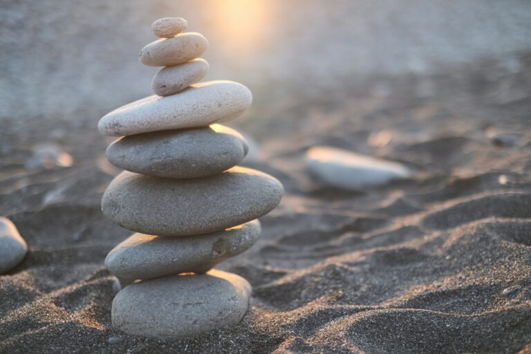 Stacked smooth stones on a sandy beach with sunlight in the background.