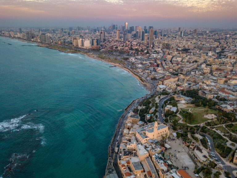 Aerial view of a coastal city with skyscrapers, historic buildings, and a sprawling beach beside turquoise sea.