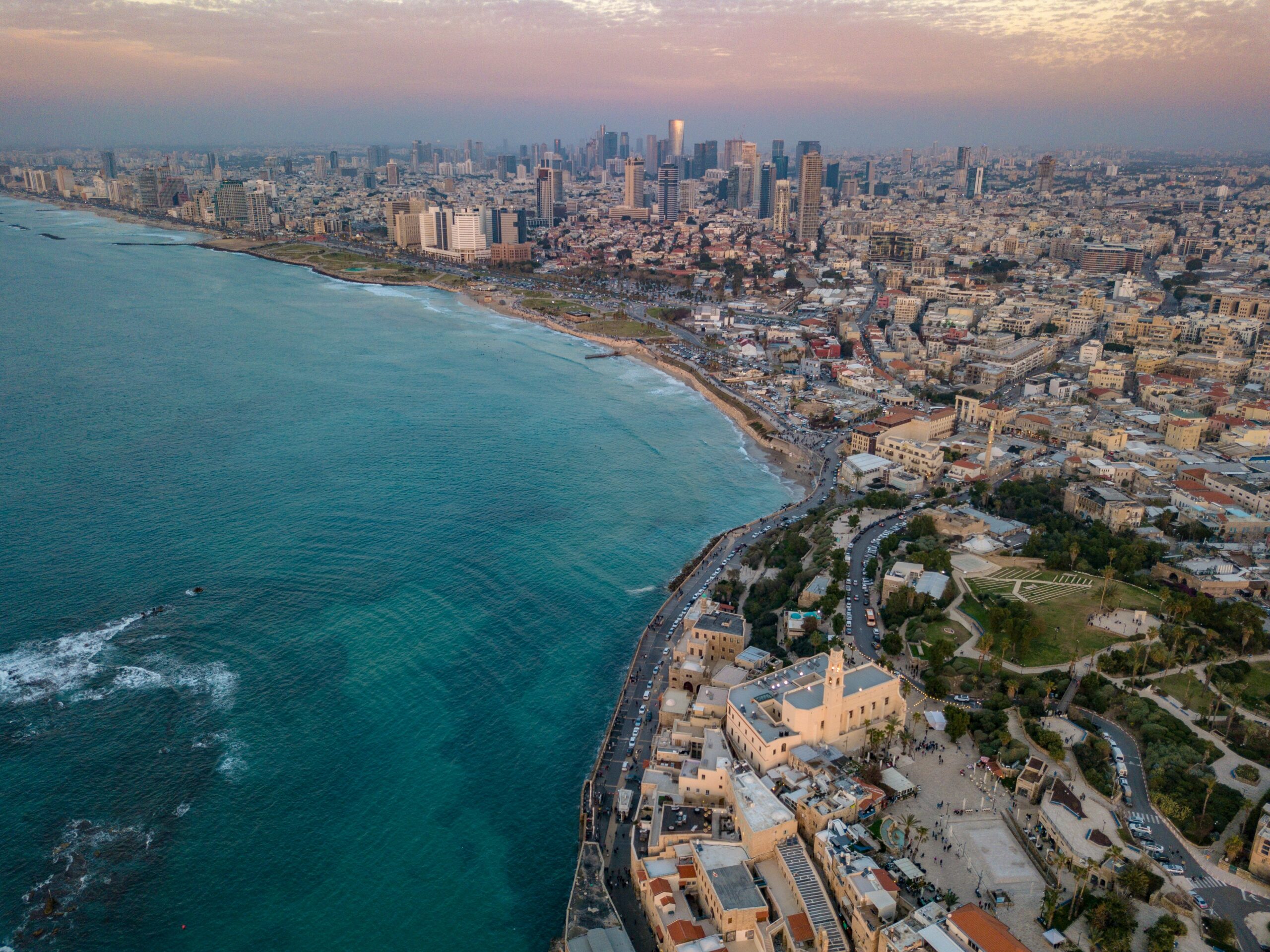 Aerial view of a coastal city with skyscrapers, historic buildings, and a sprawling beach beside turquoise sea.