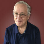 Smiling older man in a navy polo shirt against a maroon background.