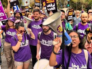 Protesters wearing purple shirts hold signs and megaphones, participating in a street demonstration.