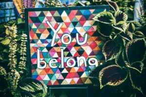 Sign with You belong on colorful triangles background, surrounded by greenery.