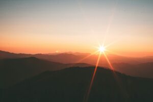 Sunrise over mountain ridges with a bright sunburst and warm orange and yellow hues in the sky.