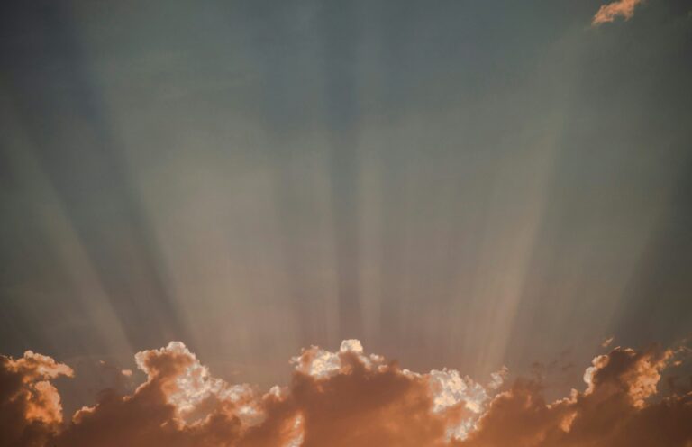 Golden clouds with sun rays streaming upward into a dusky sky.