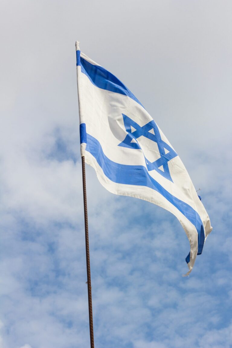 Israeli flag with blue Star of David and stripes waving against a cloudy sky.