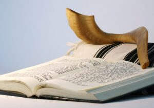 Open Hebrew prayer book with a tallit and shofar resting on top, symbolizing Jewish religious traditions.