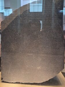 A large, dark stone slab inscribed with ancient text in three different scripts, displayed in a museum.
