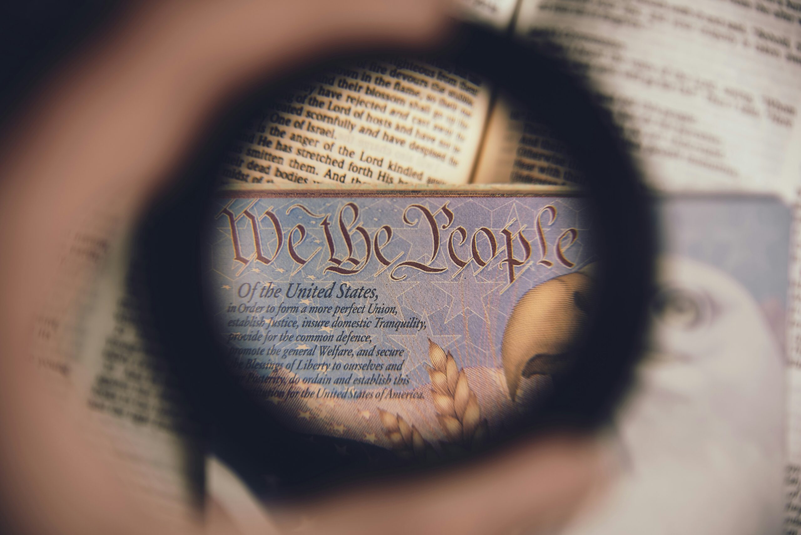 A magnifying glass focuses on the words We the People from the U.S. Constitution over an open book.