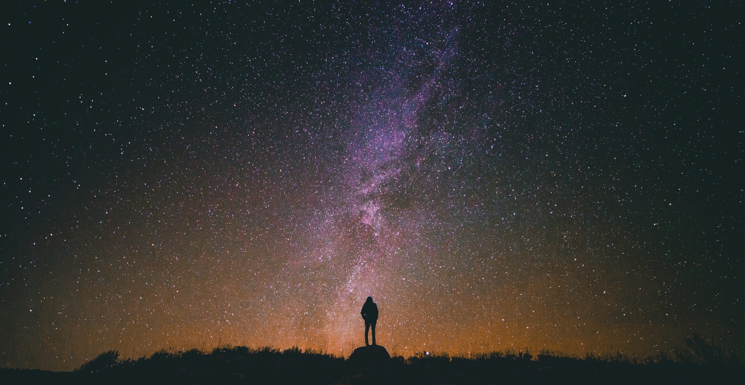 A person stands on a hill silhouetted against a star-filled night sky and the Milky Way.
