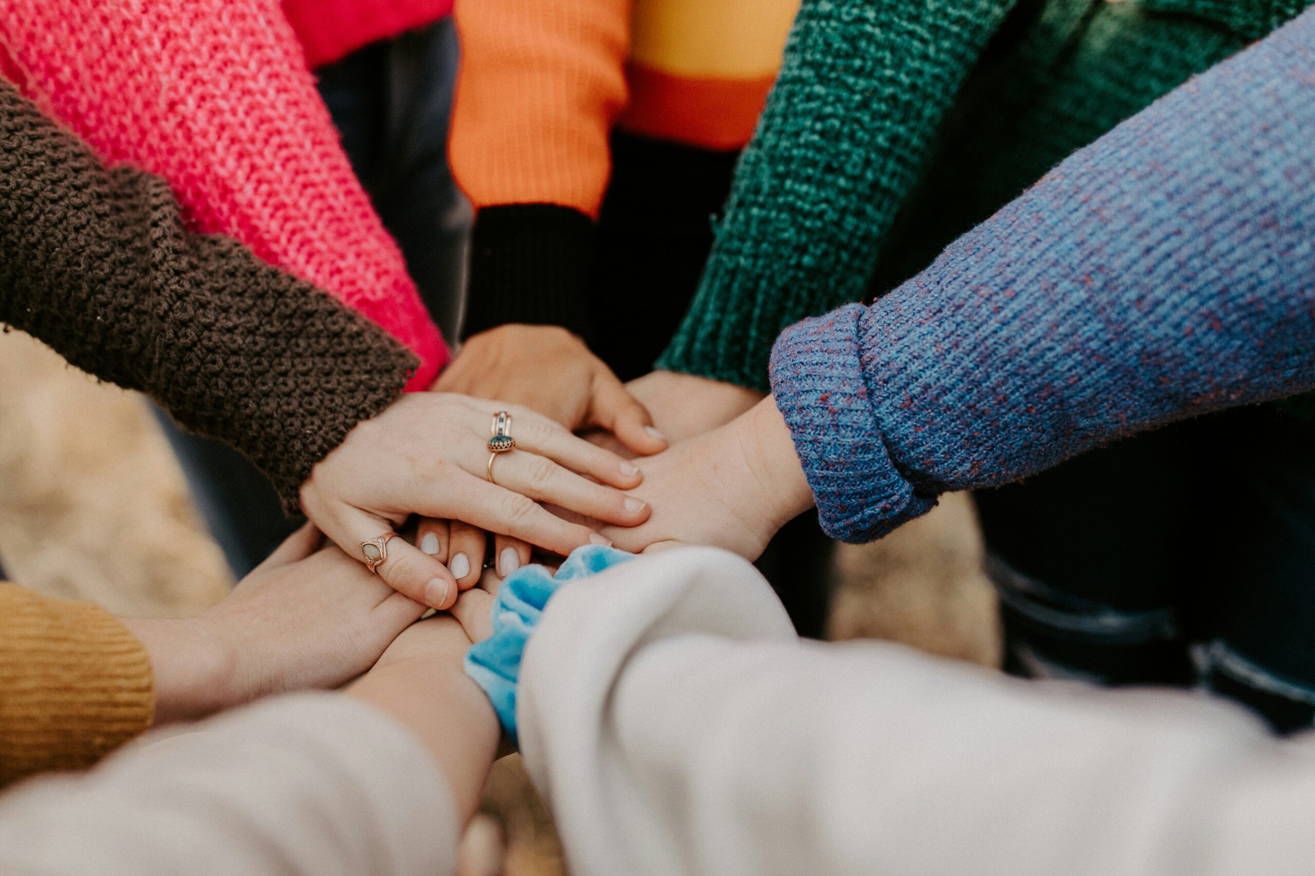 A group of people wearing colorful sweaters stack their hands together in a show of unity.