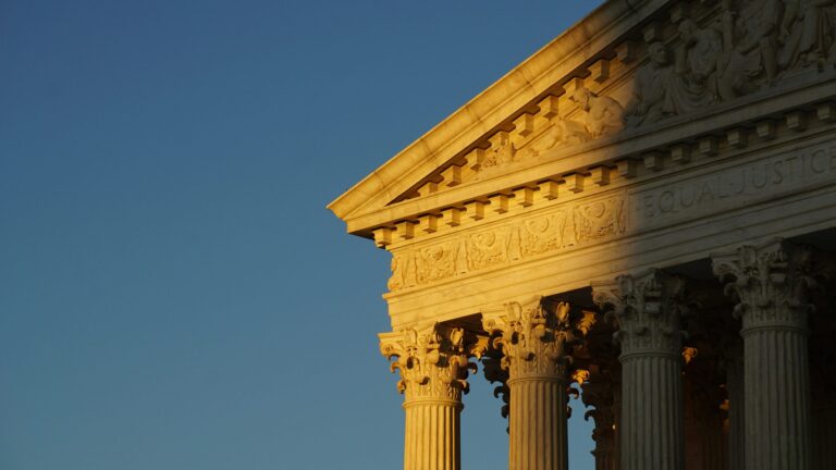 Sunlit columns and pediment of a classical building against a clear blue sky.
