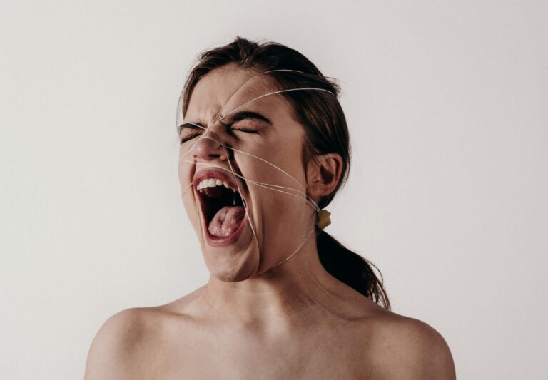 A woman screaming with strings pulling her face, against a plain white background.