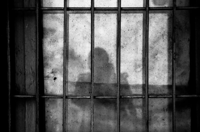 Shadowy figure behind a barred, dirty window, creating a mysterious and eerie atmosphere.
