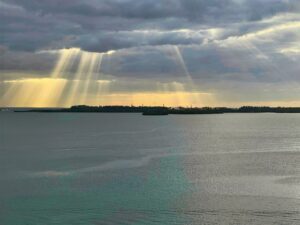 Sunbeams break through clouds over a calm body of water with distant islands on the horizon.