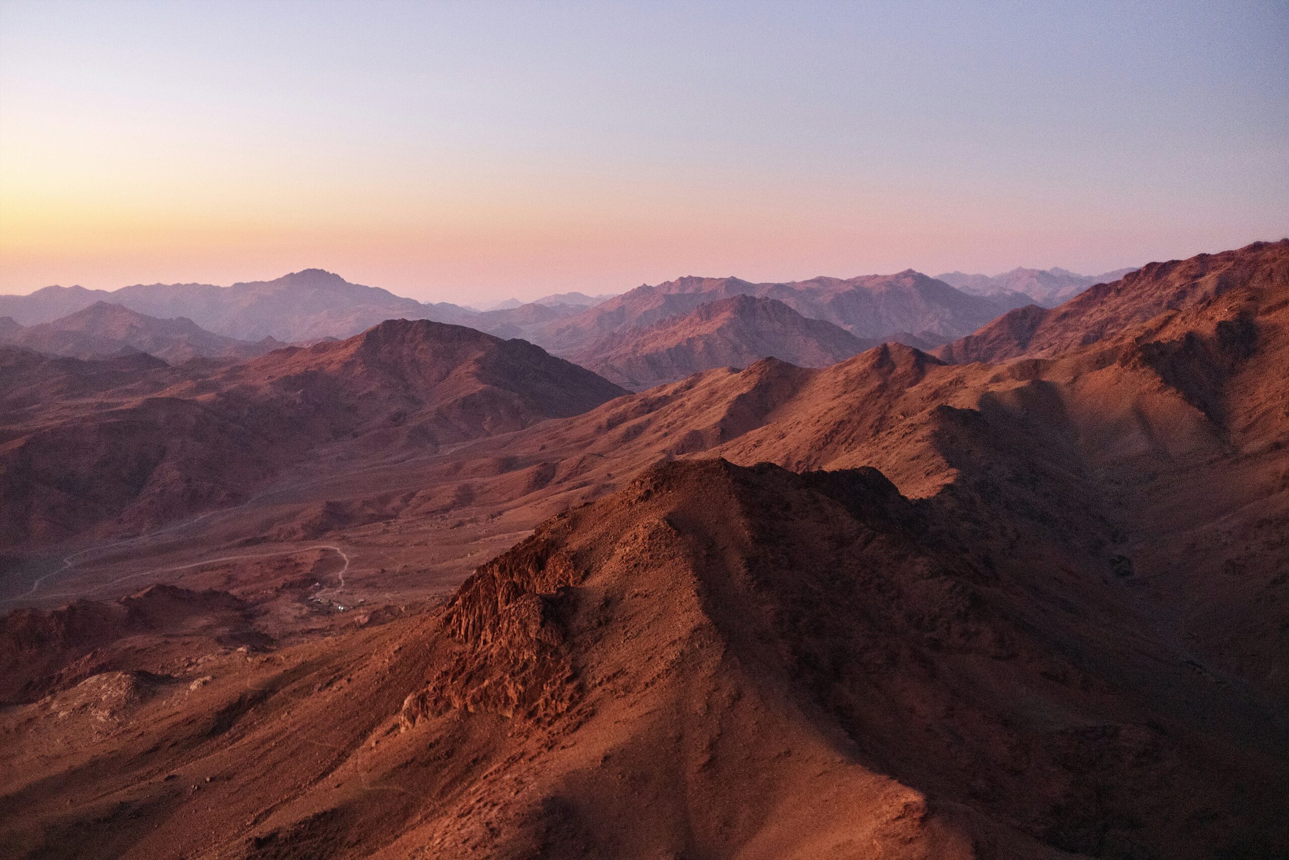 Mountain range at sunset with pink and purple hues in the sky and rugged peaks in the distance.